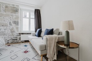 A modern living room with a stone wall, a sofa with cushions, a patterned rug, and a lamp on a stand. - Bright 1.5-room apartment in Kreis 6, roof terrace, near ETH (Zürich)