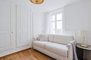 A room with a beige sofa, a round side table with a lamp, and a large window with curtains. - Bright 4.5-room apartment in Kreis 6, roof terrace, near ETH (Zürich)