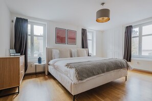 A bedroom with a bed, bedside tables, a dresser, and large windows with curtains. - Bright 4.5-room apartment in Kreis 6, roof terrace, near ETH (Zürich)