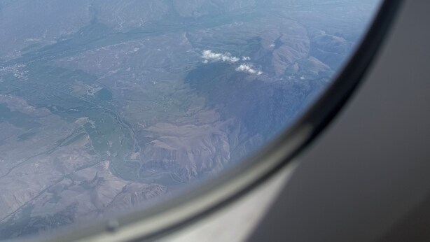 Vue par le hublot d’un avion, avec un ciel dégagé et un paysage lointain.