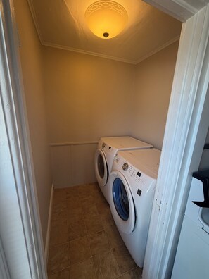 A laundry room with two stacked front-loading washing machines, a ceiling light fixture, and a tiled floor.
