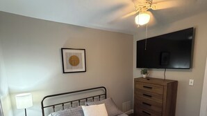 A bedroom with a bed, a bedside table with a lamp, a dresser, a ceiling fan, a wall-mounted TV, and a framed picture on the wall. - 2-bedroom fully updated and new apartment (Elmira)