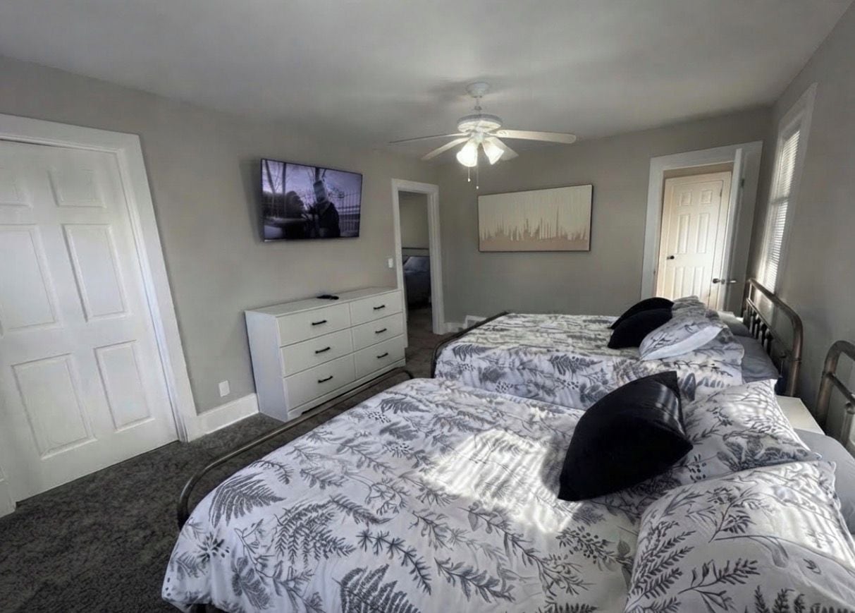 Un dormitorio con dos camas, ventilador de techo, televisión y cómoda.