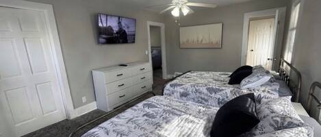Un dormitorio con dos camas, ventilador de techo, televisión y cómoda.