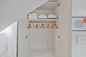 A white walk-in closet with a hanging rod for clothes and a shelf with folded towels. - Bright 4.5-room apartment in Kreis 6, roof terrace, near ETH (Zürich)