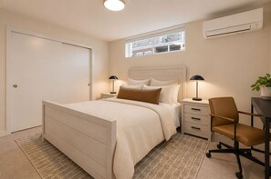 Ein Schlafzimmer mit Bett, Nachttischen, einem Sessel, einem Fenster und einer Klimaanlage.