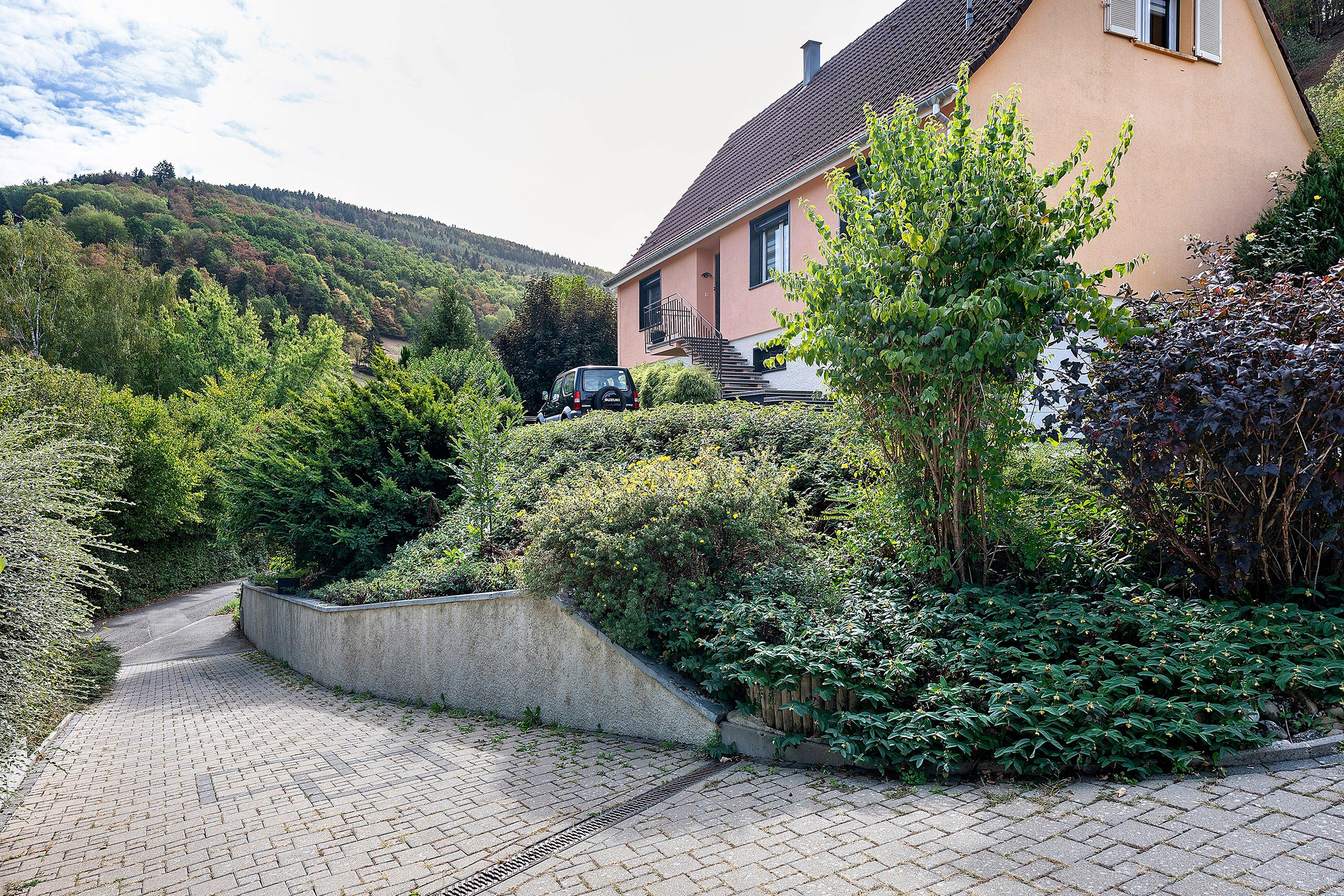 A residential property with a paved driveway, a car parked in the driveway, and a house with a sloped roof.