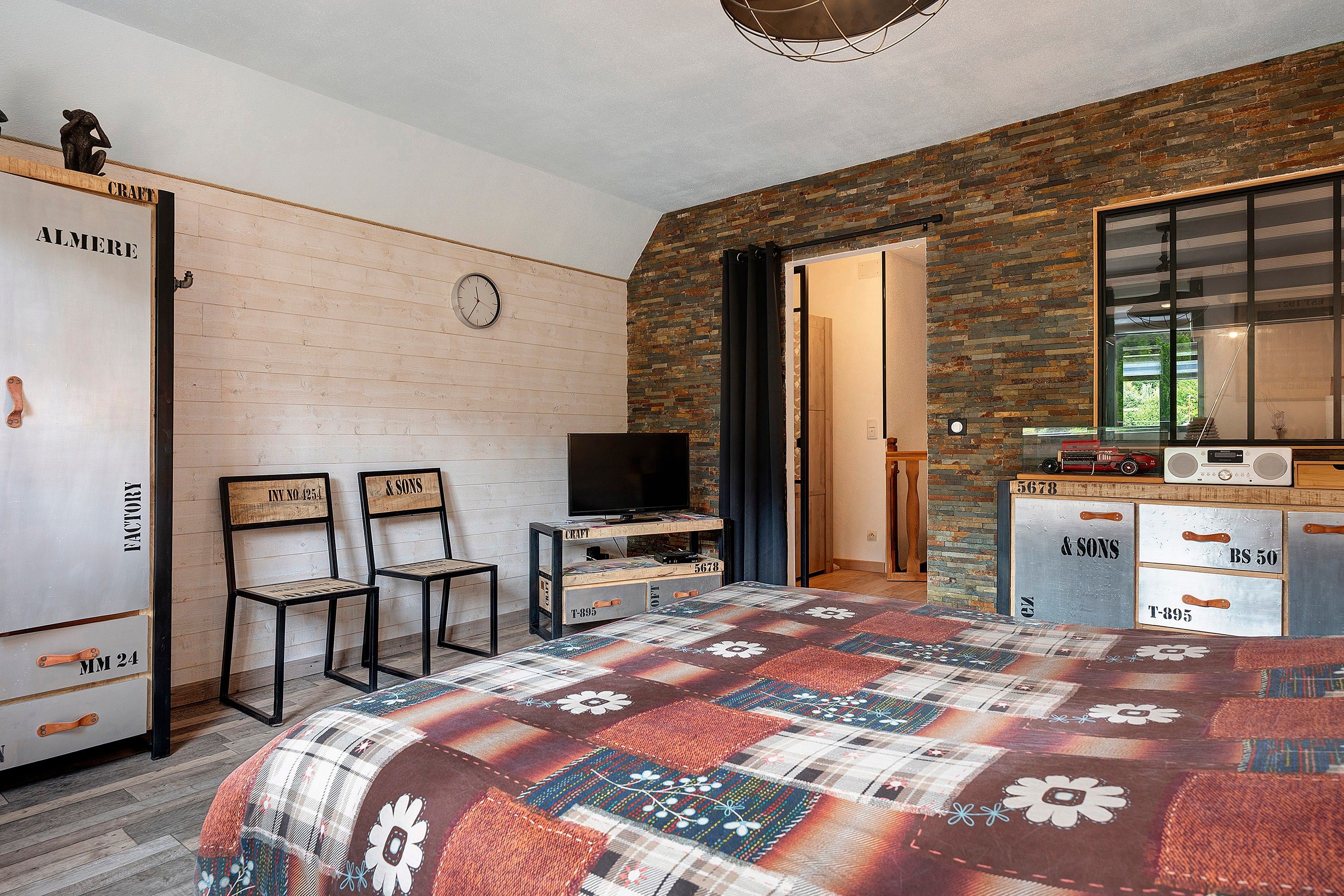 Un dormitorio con un armario de madera, televisor, escritorio con radio y colcha estampada.