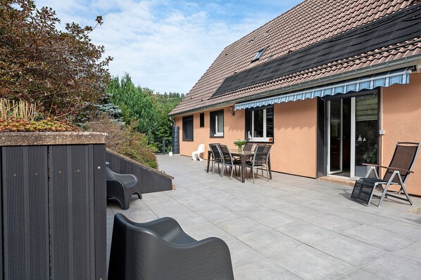 A building with a tiled roof, a patio area with chairs and a table, and a covered outdoor seating area.