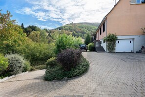Un camino pavimentado conduce a un edificio con garaje, rodeado de exuberante vegetación y un paisaje montañoso.