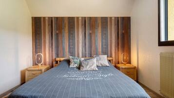 Une chambre à coucher comprenant un lit, deux tables de chevet, une fenêtre et un mur recouvert de lambris verticaux en bois.