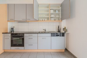 Een compacte keuken met een inbouwoven, een vaatwasser en een aanrecht met een waterkoker.