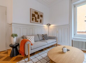 A modern living room with a grey sofa, a round wooden coffee table, and a white radiator. - Bright 3-bedroom apartment by the Limmat — tram at the door (Zürich)
