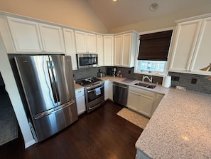 A modern kitchen with stainless steel appliances, white cabinetry, and a granite countertop. - Coastal Dream at Ortley Beach (Seaside Heights)