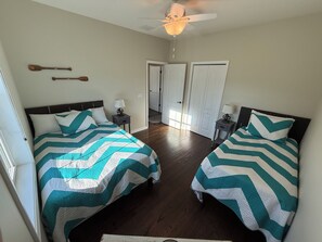 A bedroom with two beds, a ceiling fan, and a door leading to another room. - Coastal Dream at Ortley Beach (Seaside Heights)