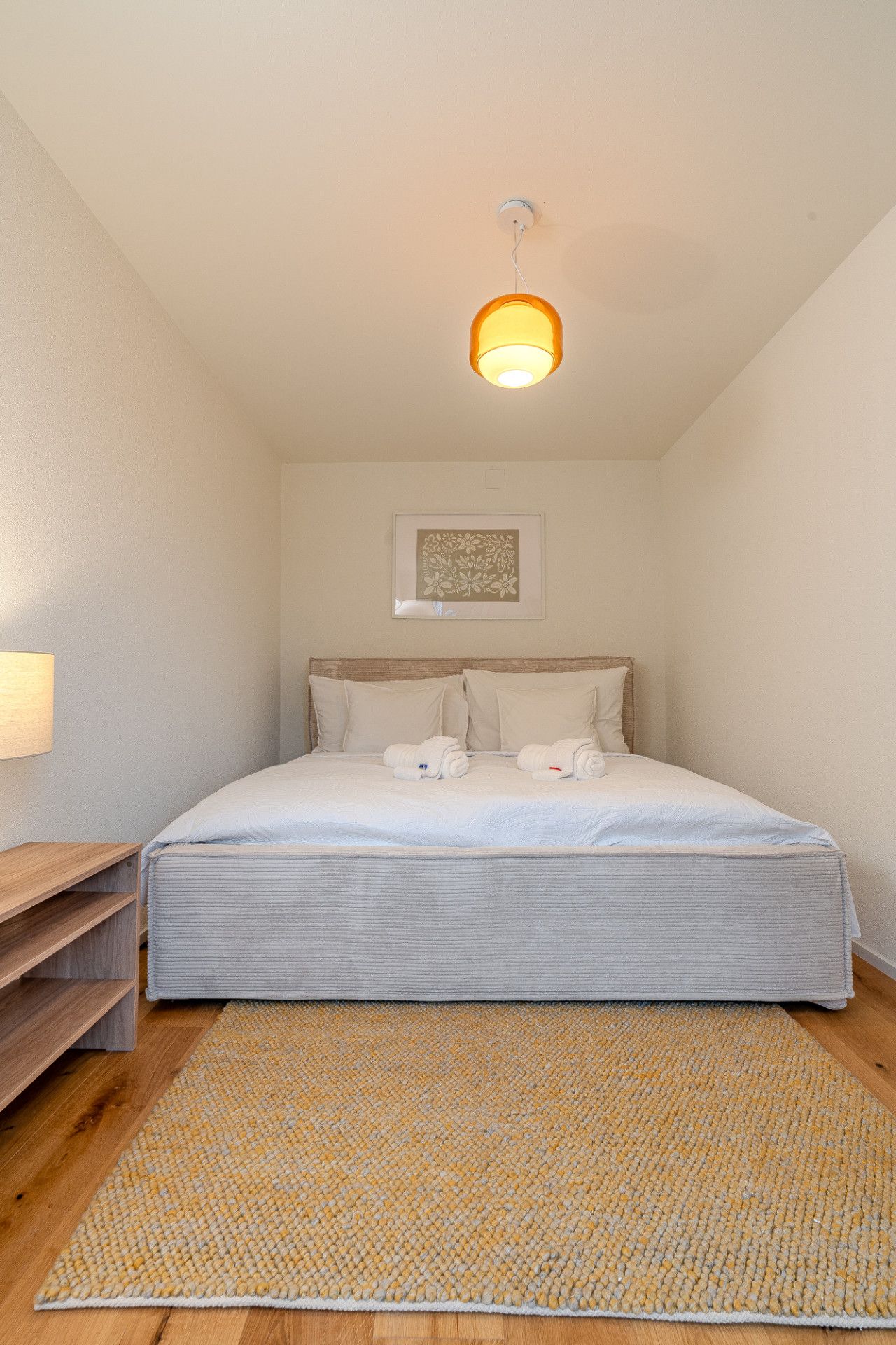 Ein Schlafzimmer mit Bett, Kissen, Kopfteil, Nachttisch, Wandleuchte und Teppich.