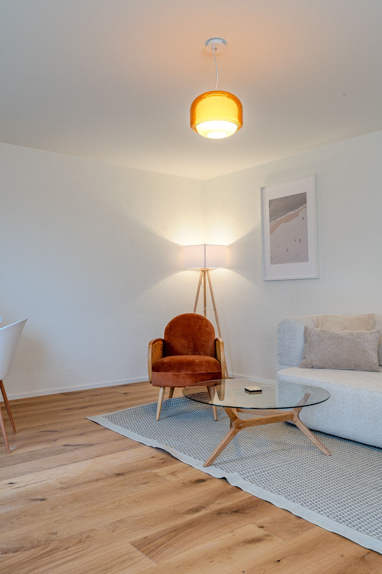 A modern living room with a wooden floor, a glass coffee table, a red velvet armchair, a white sofa, and a floor lamp.