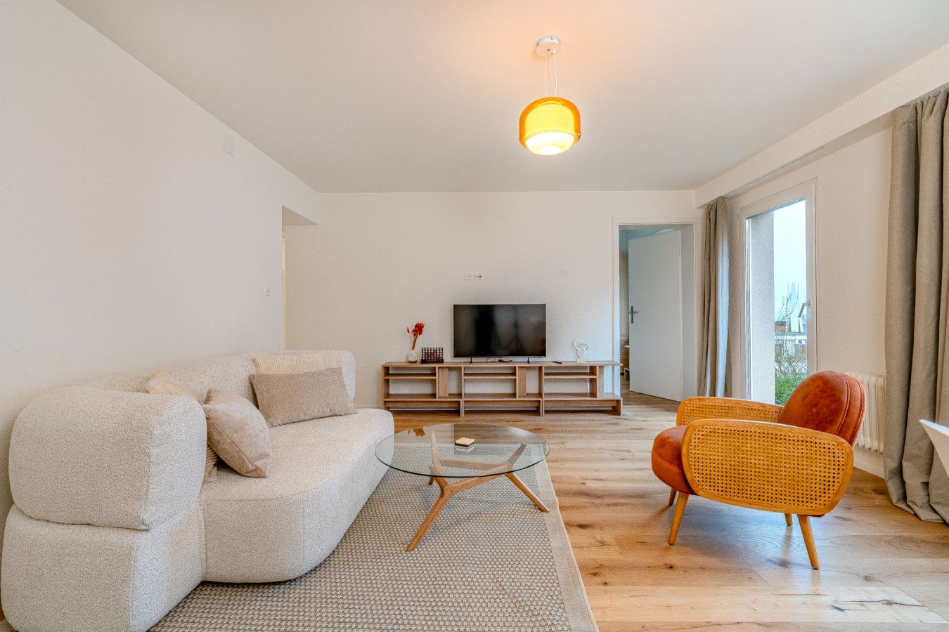 Un salon moderne avec un canapé, une table basse en verre et un téléviseur posé sur un meuble en bois.
