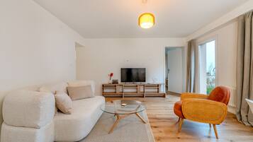 Ein modernes Wohnzimmer mit einer Couch, einem Glastisch und einem Fernseher auf einem Holzboden.