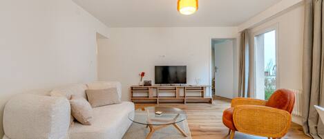 A modern living room with a sofa, a glass coffee table, and a television on a wooden stand.