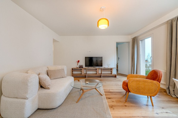 A modern living room with a sofa, a glass coffee table, and a television on a wooden stand.
