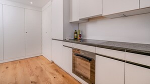 A modern kitchen with white cabinets, a stainless steel oven, and a wooden floor. - Bright 1-BR with garden view & parking · Kilchberg (Kilchberg)