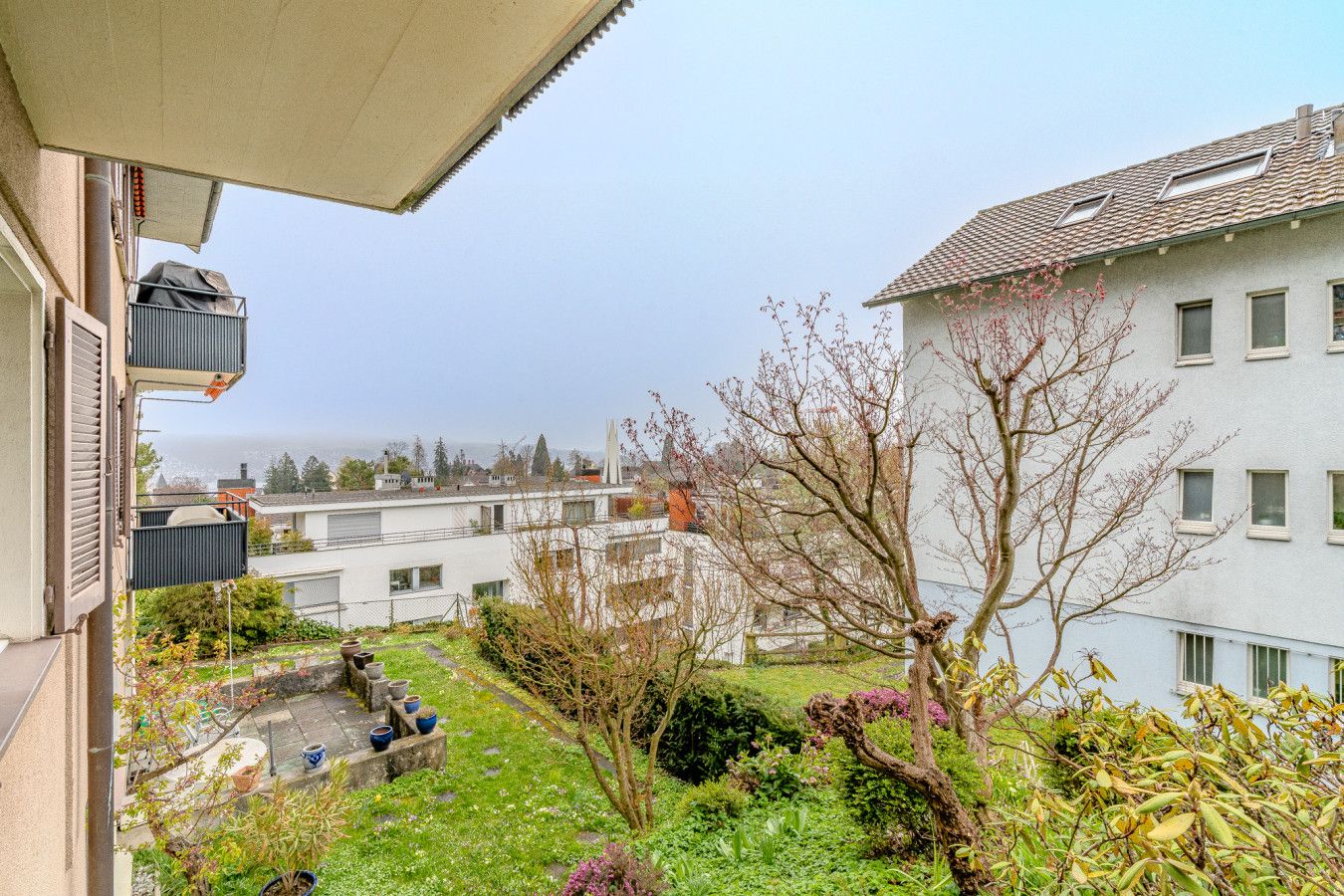 A residential area with a view of the sea, a garden with potted plants, and a building with multiple windows.