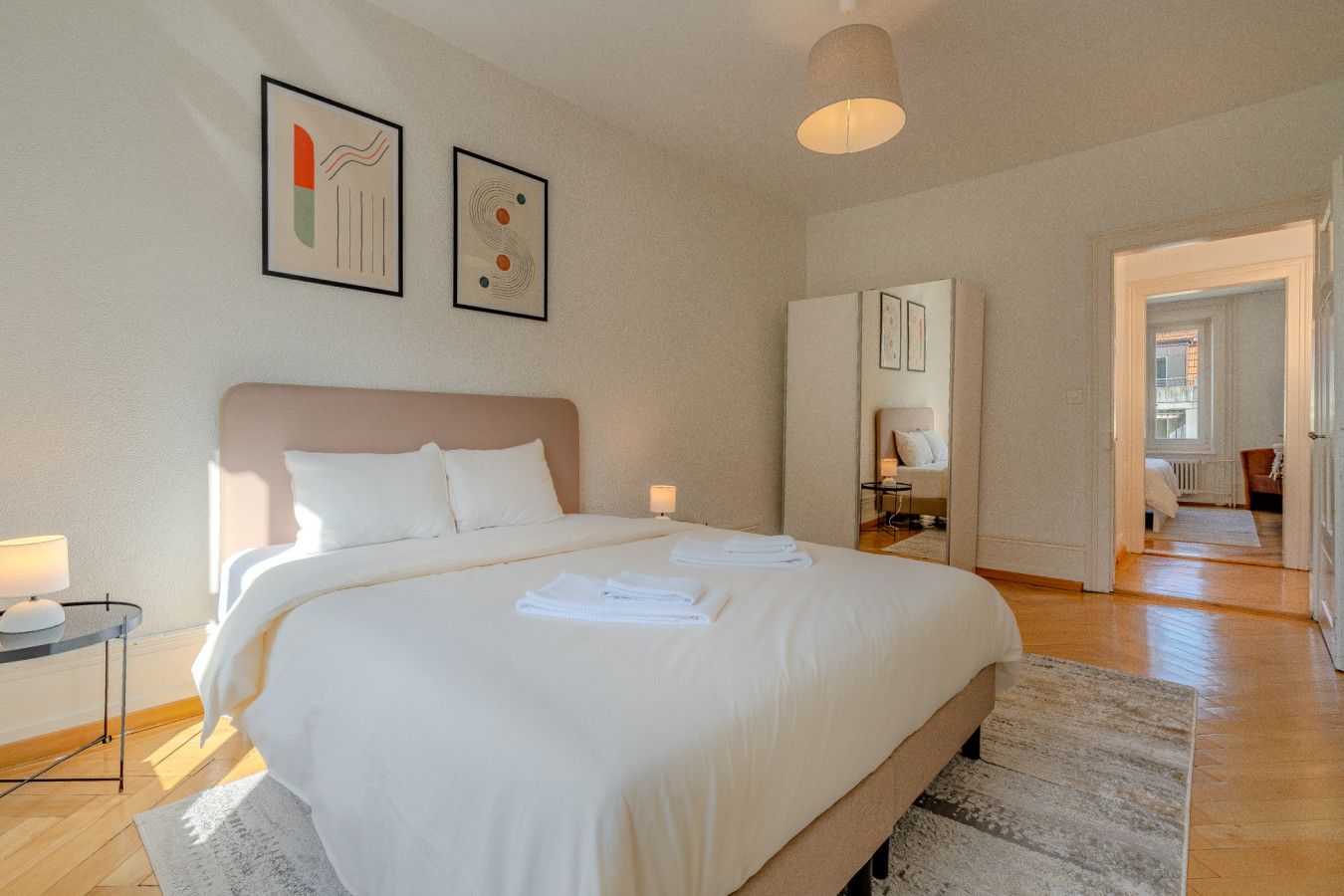 Une chambre d’hôtel avec un grand lit, une table de chevet avec une lampe et des œuvres d’art accrochées au mur.