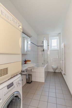 Une petite salle de bain équipée d’un lave-linge, d’un évier, d’une baignoire et de toilettes.