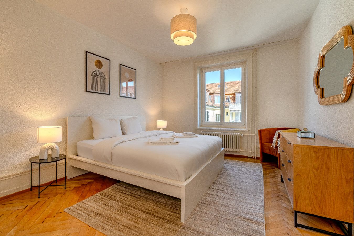 Un dormitorio con cama, lámparas de noche, cómoda, ventana y una obra de arte en la pared.