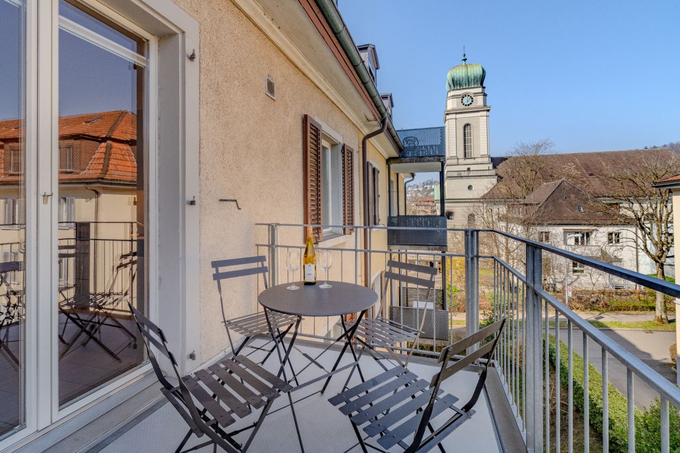 Un balcon avec une table et des chaises, donnant sur un bâtiment doté d’un clocher.