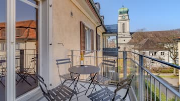 Un balcon avec une table et des chaises, donnant sur un bâtiment doté d’un clocher.