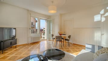 Un salon spacieux avec un téléviseur, un coin repas avec des chaises, un canapé et une table basse en verre.