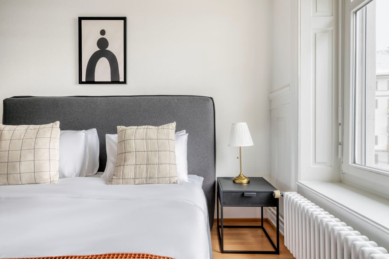 Un lit bien fait, avec une tête de lit, une table de chevet avec une lampe et un radiateur.