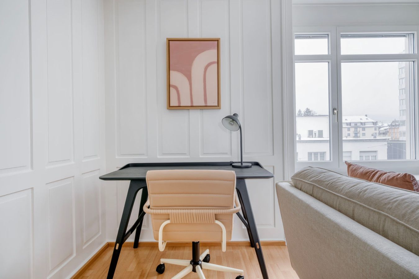 A modern office space with a desk, office chair, and a view of buildings through a large window.