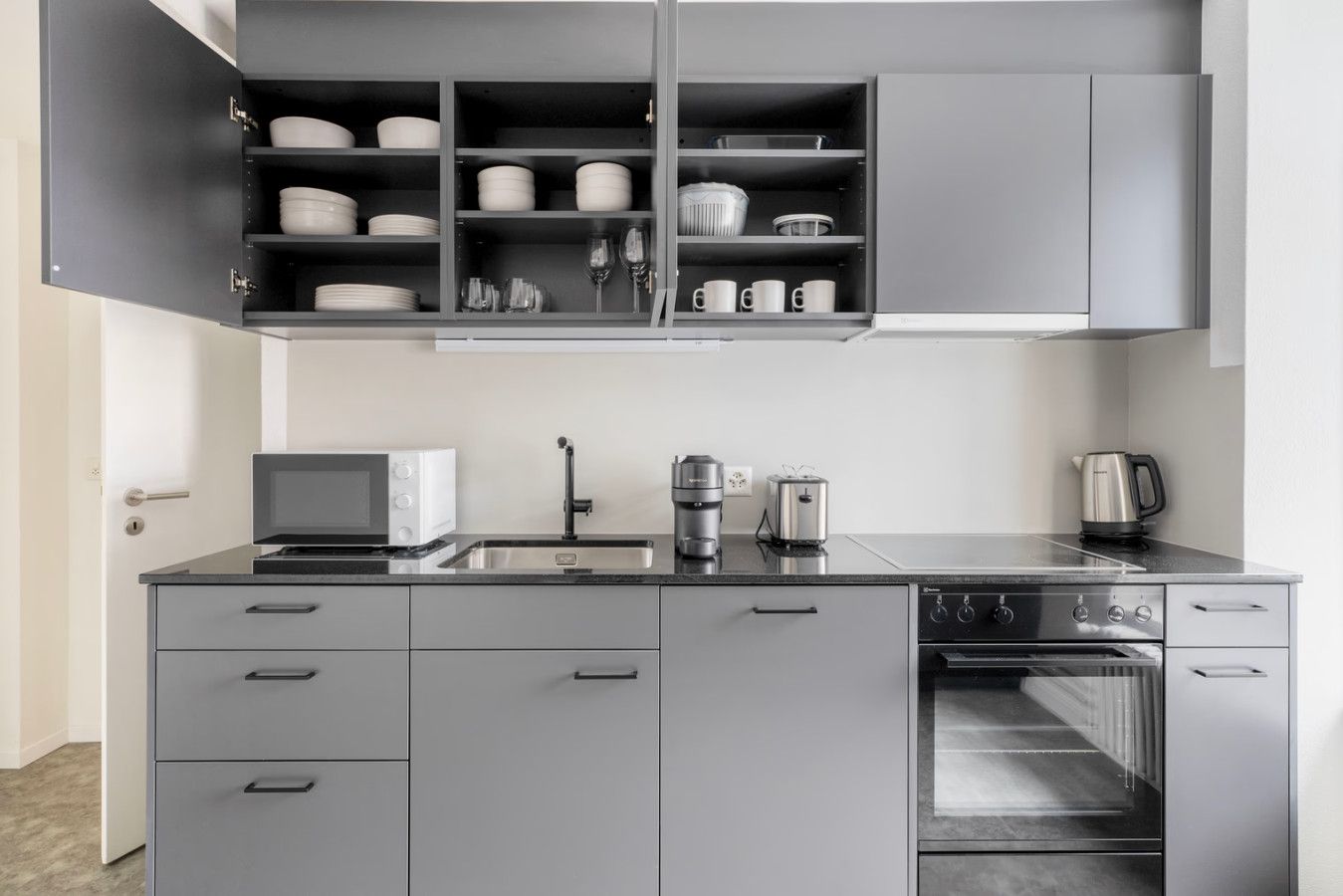 A modern kitchen with grey cabinetry, a built-in oven, a coffee maker, and a microwave.