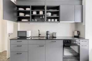 Eine moderne Küche mit grauen Schränken, einem eingebauten Backofen, einer Kaffeemaschine und einer Mikrowelle.