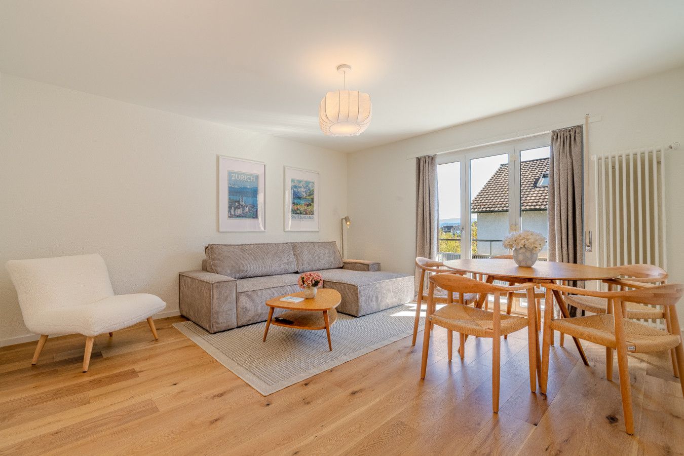 Ein modernes Wohnzimmer mit einer Couch, einem Esstisch mit Stühlen, einem Couchtisch und einer Hängeleuchte.