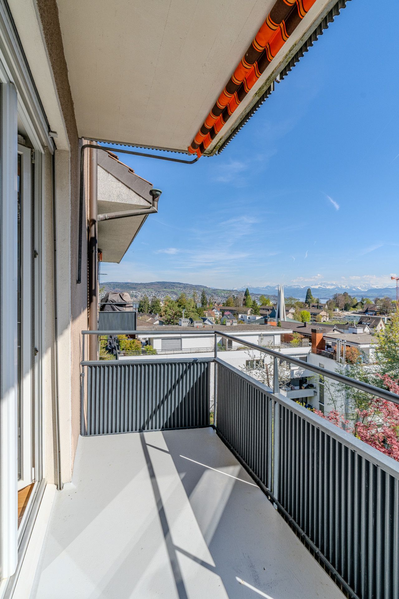 Ein Balkon mit Metallgeländer, Blick auf eine Stadt und ein klarer Himmel.