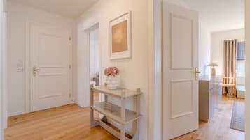 Un pasillo con una puerta blanca, un estante blanco con un jarrón de flores y un cuadro en la pared.