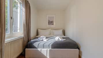 Un dormitorio con cama, un radiador, una ventana con cortinas y un cuadro en la pared.