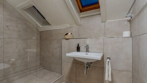 Ein modernes Badezimmer mit Dachfenster, einem Waschbecken und einer Duschkabine aus Glas.