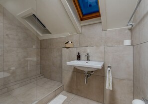 Een moderne badkamer met dakraam, een wastafel en een douchecabine van glas.