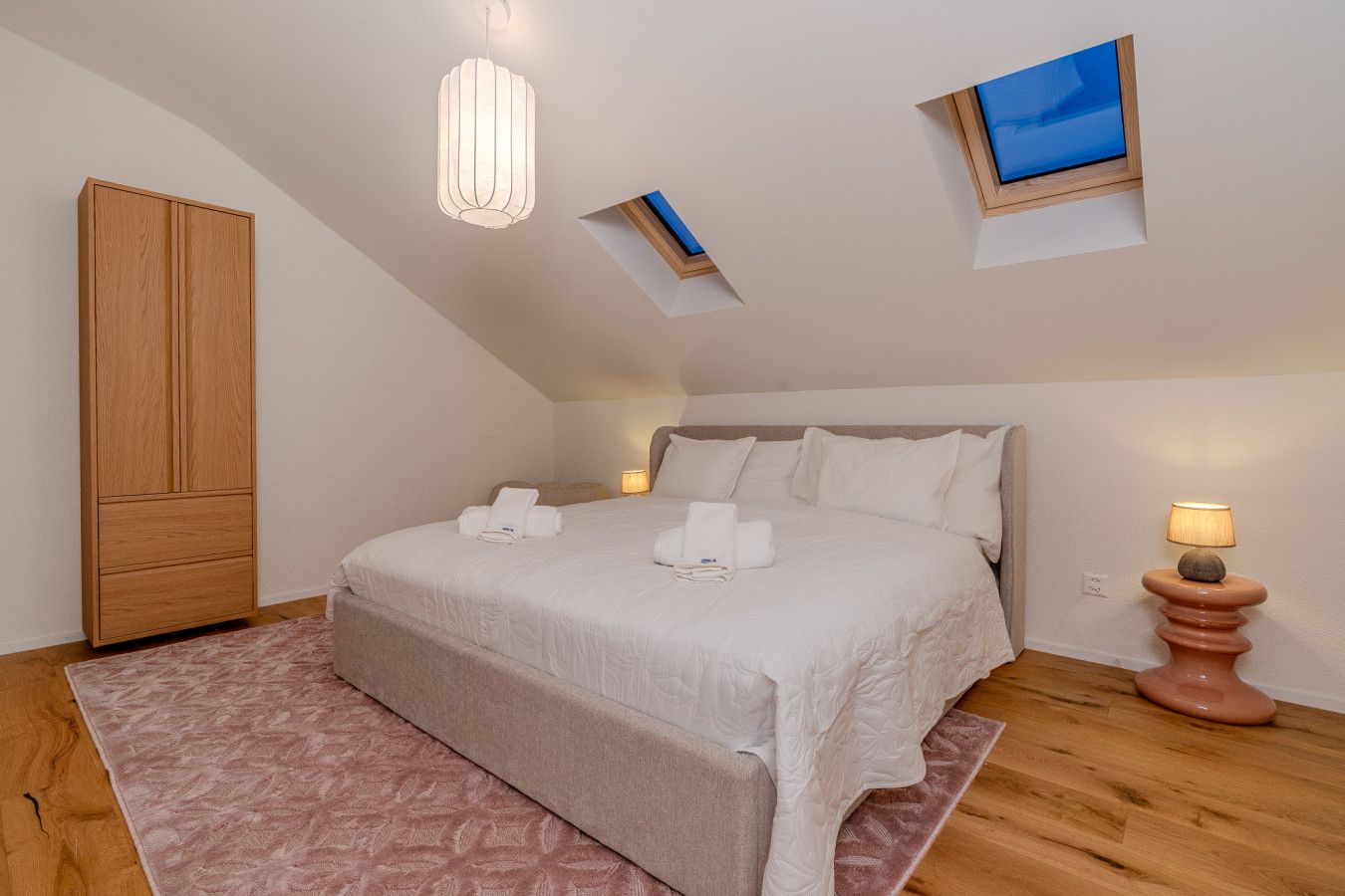 Ein Schlafzimmer mit einem großen Bett, einem Kleiderschrank, einem Nachttisch mit Lampe und einem kleinen Fenster mit Blick.