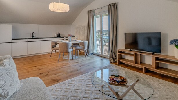 Ein modernes Wohnzimmer mit einem Glastisch, einem Flachbildfernseher und einem Essbereich mit Tisch und Stühlen.