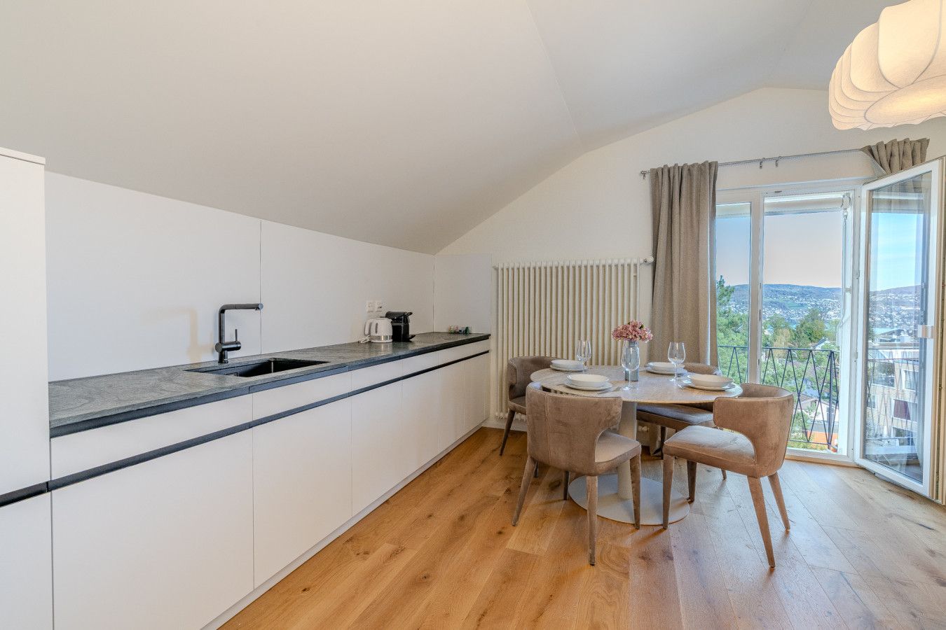 A modern kitchen with a dining area, a large window with a view, and a built-in oven.