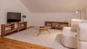 Ein modernes Wohnzimmer mit Flachbildfernseher, Holzmöbeln, einem runden Glastisch und einer Deckenleuchte.