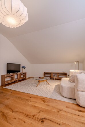 Een moderne woonkamer met een flatscreen televisie, houten meubels, een ronde glazen tafel en een plafondlamp.