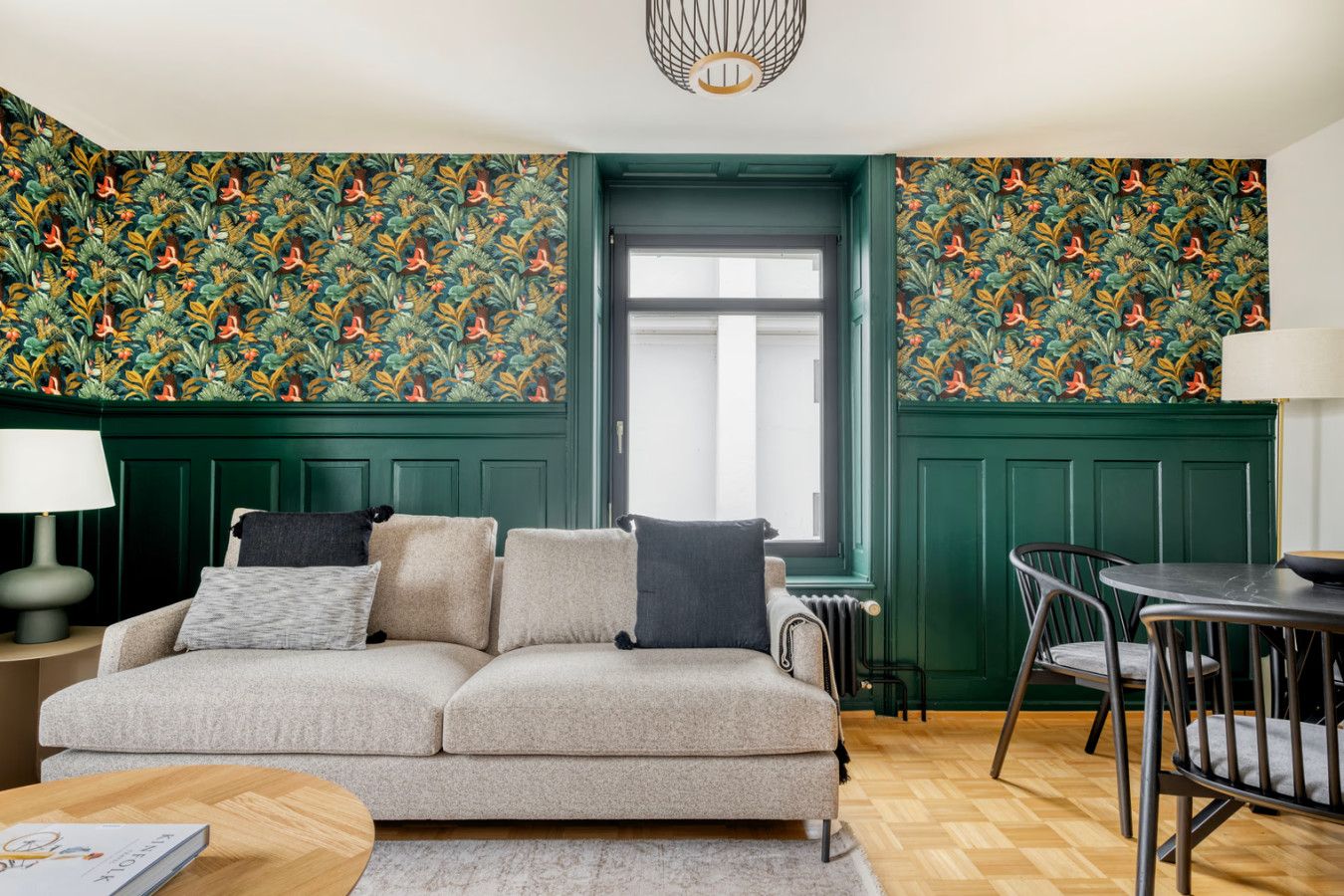 Un salon avec un canapé, une table et des chaises. Il y a une fenêtre qui donne sur l’extérieur.