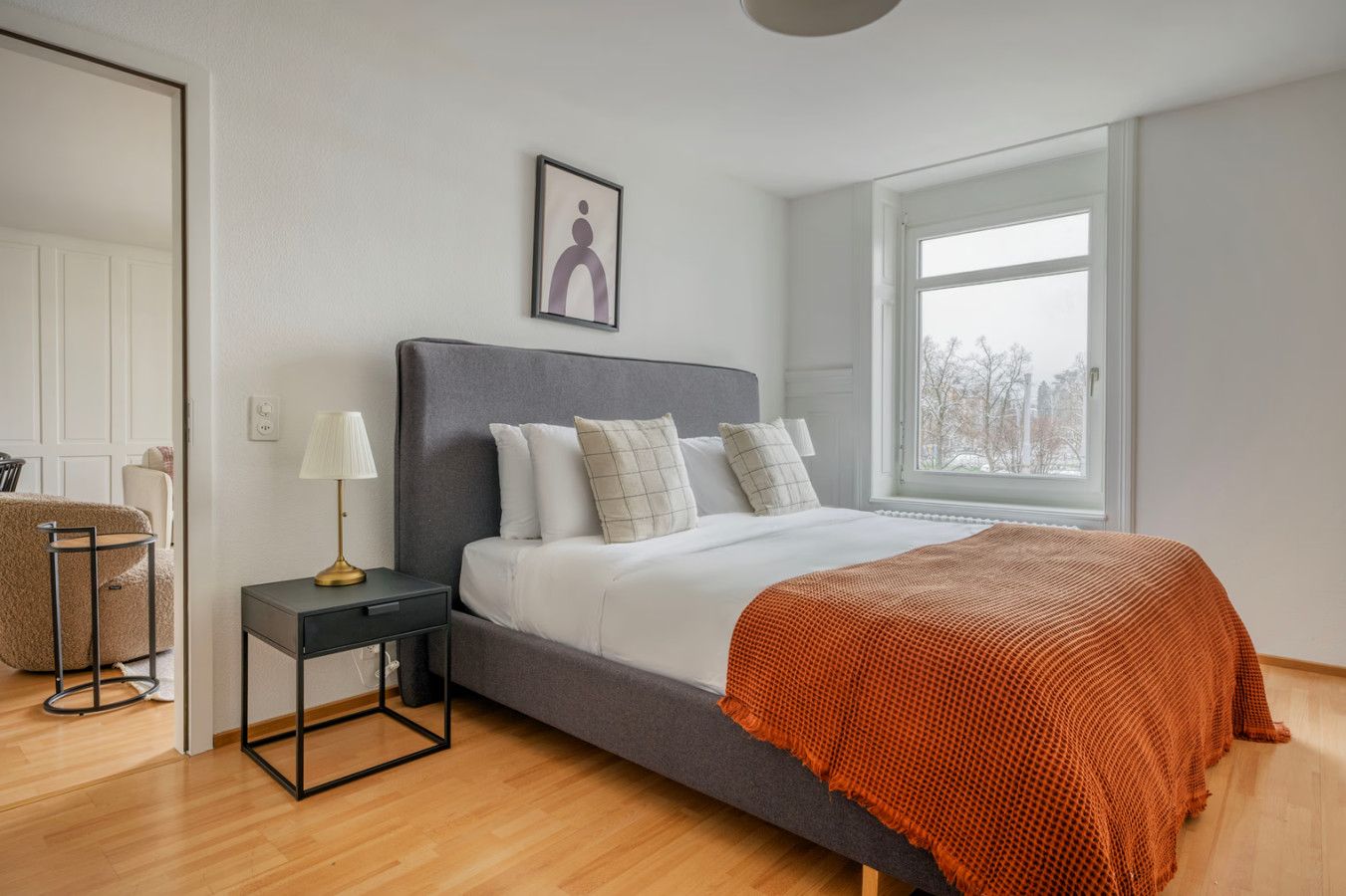 A modern bedroom with a large bed, a bedside table, a lamp, and a window.
